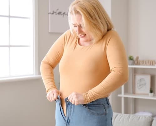 Using the Be Do Have coaching model, this woman will be able to lose weight and do up her jeans. Young woman struggles to get into her jeans because of weight.