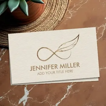Business card example for life coaches with a gold infinity symbol and feather logo above the name Jennifer Miller on a textured cream background, styled for a professional title or life coach