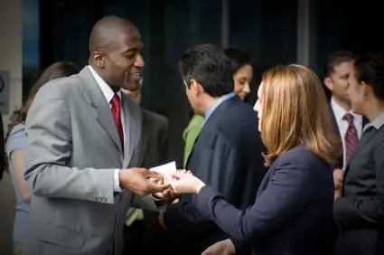 Businesswoman handing a business card at a networking event, demonstrating marketing ideas for life coaches to create client opportunities